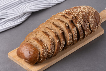 Freshly sliced sesame seed bread on a wooden cutting board with a striped kitchen towel in the background in a modern kitchen