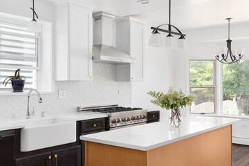 A kitchen detail with wood and white cabinets, a light wood island with a marble countertop, tiled backsplash, stainless steel appliances, and a chrome faucet on a white farmhouse sink.