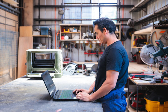 Latin carpenter working on laptop in workshop - Powered by Adobe