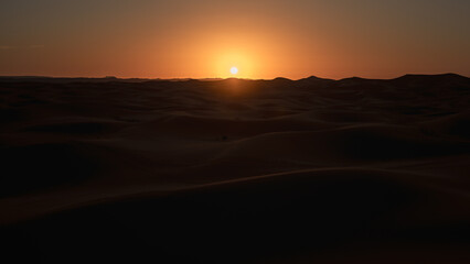 Sun setting behind the sand dunes of erg chebbi near merzouga, creating a beautiful orange glow in the sahara desert, morocco