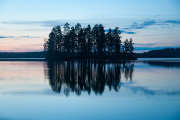 Fototapeta premium Late evening scenery of a calm lake with a wooden island in the forests of Finland