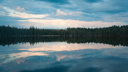 Fototapeta premium Clouds and forests reflected on the surface of a calm lake in Finland