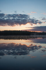 Fototapeta premium Clouds and forests reflected on the surface of a calm lake in Finland