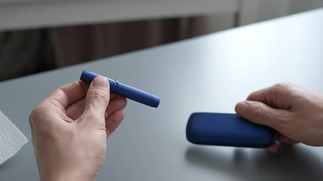 Close-up revealing heated tobacco stick insertion into sleek iqos electronic cigarette device. Concept of contemporary smoking alternative method. Shooting in slow motion.