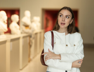 Museum female visitor walk through exhibition halls museum. Girl inspects sculpture of various...