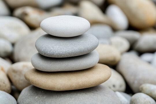 White stones stacked in balance on beach with smooth pebbles background. Slow life, balance, mindfulness, and harmony concept