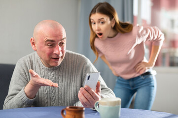 Angry and jealous wife observing her husband using smartphone.