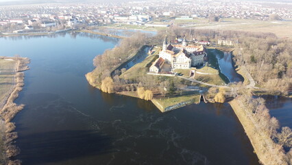 View from drone of impressive medieval palace and park ensemble surrounded by ponds in Belarusian city Nyasvizh on winter day..