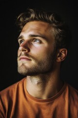 Obraz premium A man with a beard and a blue shirt is looking up at the camera. The image has a warm and friendly mood, as the man's smile and the orange shirt create a sense of approachability and positivity