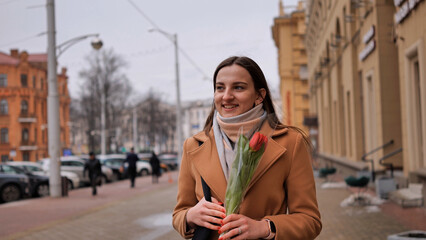 Obraz premium Portrait of a happy shade girl with a tulip in the background of the city in the cold season.
