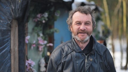 Homeless man smiling beside makeshift shelter, constructed from plastic sheets, adorned with artificial floral decorations
