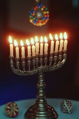 A lit menorah with candles on it sits on a table. The candles are lit and the menorah is surrounded by a colorful candy wreath