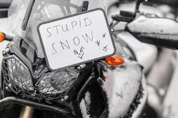 A large black touring motorcycle is covered in snow. The end of the motorcycle season, winter. The...