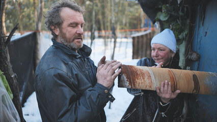 Homeless pair sharing warmth near rusty pipe, surviving harsh winter conditions in dilapidated...