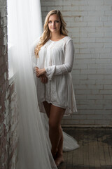 Fototapeta premium Sexy young blonde woman stands near window wearing lace dress