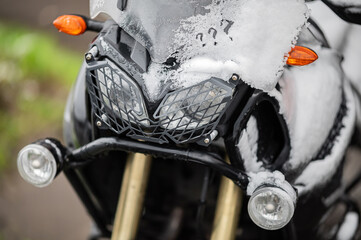 A large black touring motorcycle is covered in snow. The end of the motorcycle season, winter. The...