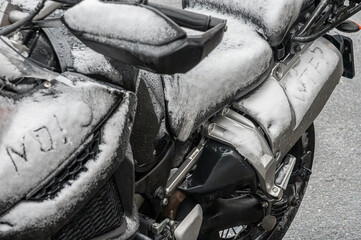 A large black touring motorcycle is covered in snow. The end of the motorcycle season, winter. The...