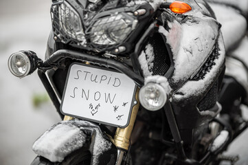 A large black touring motorcycle is covered in snow. The end of the motorcycle season, winter. The...