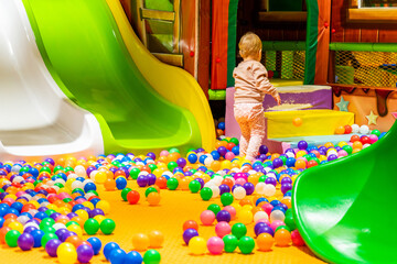 A joyful toddler exploring a colorful indoor playground with slides and a ball pit.