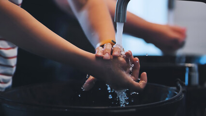Children washing hands thoroughly, practicing good hygiene at bathroom sink with running water and antibacterial soap