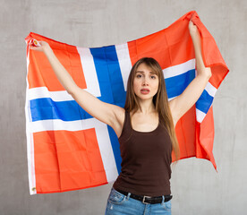 Sad young woman with large flag of Norway posing sorrowfully against light unicoloured background