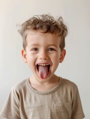 A playful young child with curly hair joyfully sticks out his tongue, expressing a moment of carefree happiness. His bright eyes and cheerful demeanor showcase youthful innocence and exuberance.