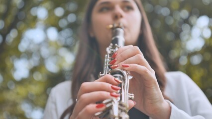Fototapeta premium Female musician performing clarinet amid lush greenery, expressing musical passion through melodic outdoor performance