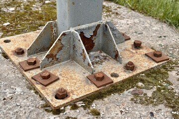 Metal pillar fastened to basement with anchor bolts and nuts. The rusty surface of the post and the...