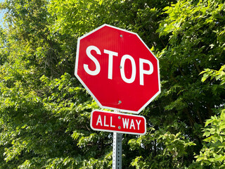 Red and white octagonal stop sign with all way sign below, against a backdrop of vibrant green...