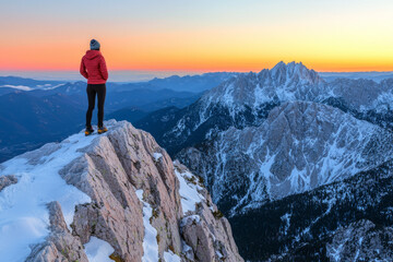 Naklejka premium Hiker on snowy peak, sunset over vast mountain range.