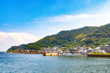 This is a beautiful image of the East China Sea shoreline. The lush green rolling hills on the banks look pretty set against the sky with white clouds. This image was taken from Nagasaki, Japan.