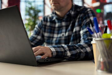Freelancer at home office desk using laptop to compose social media posts, producing content. Close up of remote worker using notebook to monitor company social media engagement