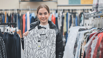 Smiling shopper gripping shirt hanger, browsing clothing store filled with vibrant fashion selections