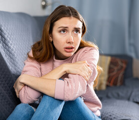 Portrait of a frustrated young European woman sitting on a sofa in an apartment