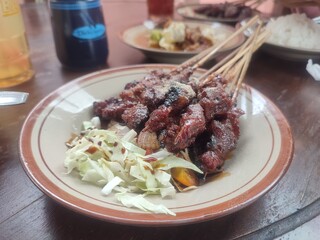 Goat satay is an Indonesian dish made of skewered and grilled goat meat, served with soy sauce, peanut sauce, or spicy sambal for a rich, savory flavor.