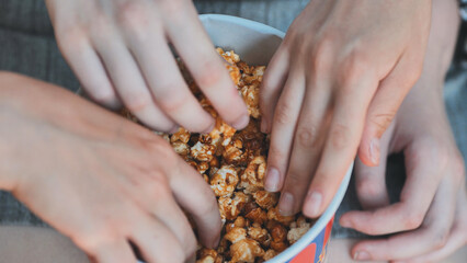 Hands grabbing caramel popcorn during sunny park gathering, friends sharing tasty treat outdoors