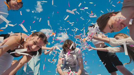 High school graduates joyfully tossing colorful confetti in the air under a vibrant summer sky