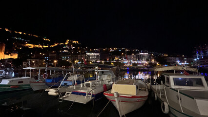 Boats Docked At A Nighttime Marina With Illuminated Hillside Buildings In The Background, Alanya Harbor, Evening Cityscape Concept, Suitable For Travel Agencies, Tourism, And Marketing Materials.