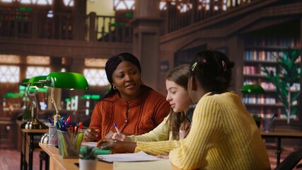Black teacher mentoring her teen girls students with an assignment, teaching academic concepts and enhancing their knowledge through practical exercises. Private lessons at the library. Camera B.