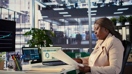 Black influential businesswoman evaluates company performance, using data reports and analytics to...