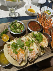 Close-up of gourmet lobster tacos topped with cilantro, served with fresh salsa, guacamole, and lemon wedges on a wooden board, showcasing elegance, concept of fine dining, culinary art, lifestyle