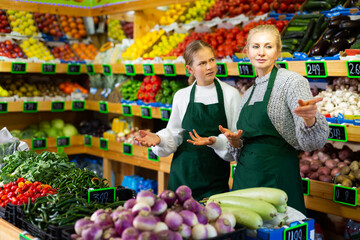 Dissatisfied young salesgirl listening to directions from experienced female colleague while...
