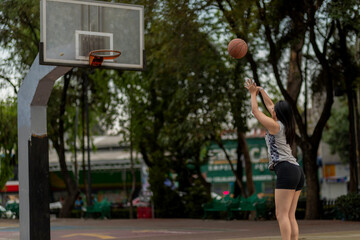 Young woman throwing basketball into hoop on outdoor court