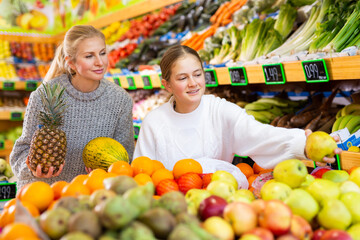 Mom and her teen daughter pick pineapple and melon at the grocery supermarket