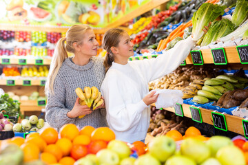 Positive woman and teenage girl shopping vegetables and fruits at the grocery shop