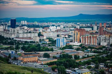 Obraz premium Krasnoyarsk, russia, city skyline featuring residential and industrial buildings at sunset with a mountain in the background