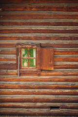 Traditional russian log cabin showcasing weathered wooden wall with a small, partially opened window revealing a vase of flowers inside