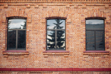 Obraz premium Arched windows reflecting lush trees on a textured brick wall of a building in russia, creating a picturesque urban scene