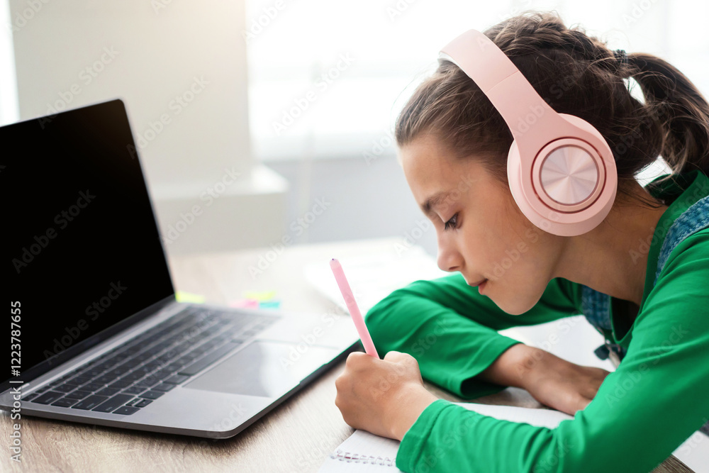 Poster side view profile of focused little girl writing down information watching webinar on laptop with em