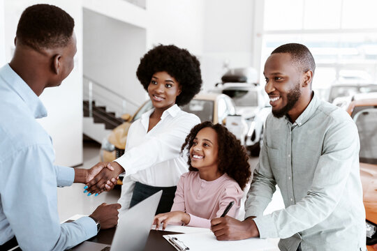 Its a deal. Positive black family buying new car, shaking hands with salesman, signing auto purchase agreement at dealership. Cheerful Afro clients shopping for automobile at automotive showroom - Powered by Adobe